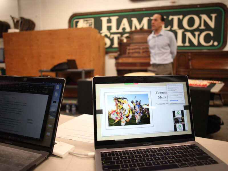 Two laptops on a desk, with one displaying a live online learning video call with multiple participants and the guest speaker being videoed in the background.