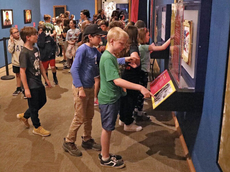 A group of elementary school students standing in a museum gallery, looking at an educational exhibit during a school visit to Museum of the Rockies.