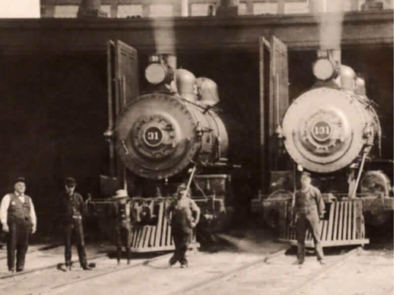 A historical black-and-white photograph of two Northern Pacific Railroad steam engines parked side-by-side, with railroad workers standing on the ground in front of them.